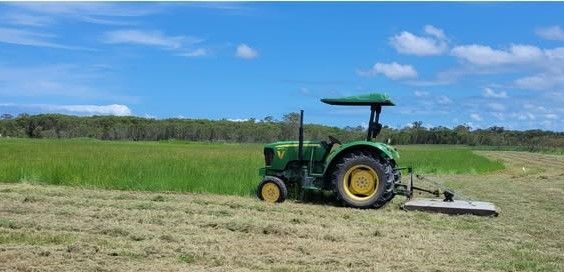 A Green Tractor is Cutting Grass in a Field — CQ Rural Services In Bakers Creek, QLD