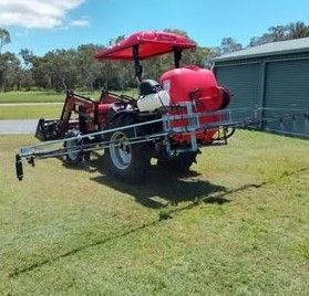 A Red Tractor With a Sprayer Attached to It is Parked in a Grassy Field — CQ Rural Services In Bakers Creek, QLD