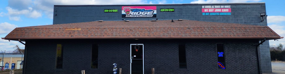 A dark brick building with a brown roof, featuring storefront windows and a sign that reads 