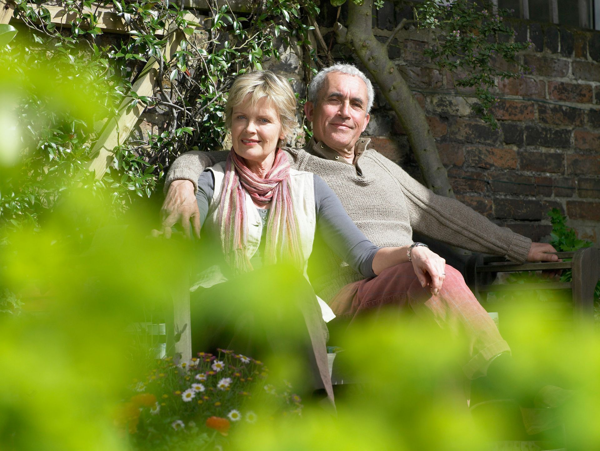 Couple sitting outdoors, arm around each other, smiling, surrounded by greenery.