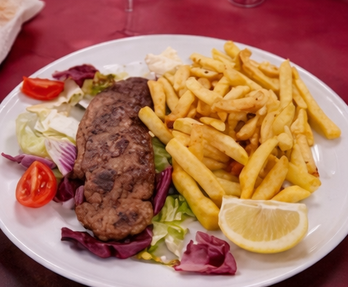 Un piatto con hamburger di carne grigliati, patatine fritte, lattuga fresca, cavolo rosso, pomodorini e uno spicchio di limone.
