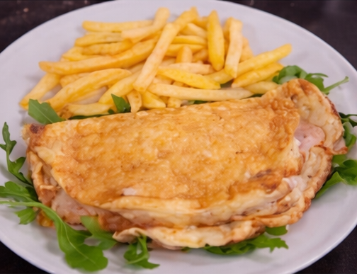 Una frittata ripiena di prosciutto e formaggio, servita su un letto di rucola fresca con contorno di patatine fritte croccanti su un piatto bianco.