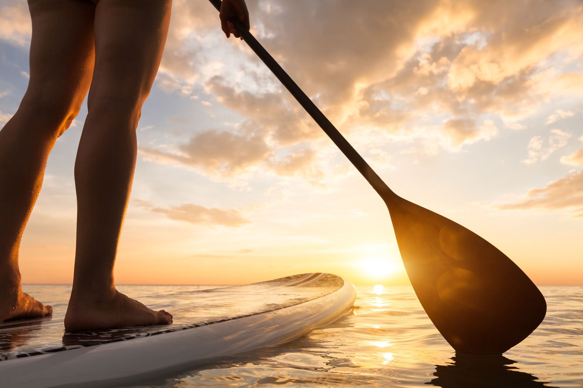 Stand up paddle boarding on a quiet sea with warm summer sunset colors