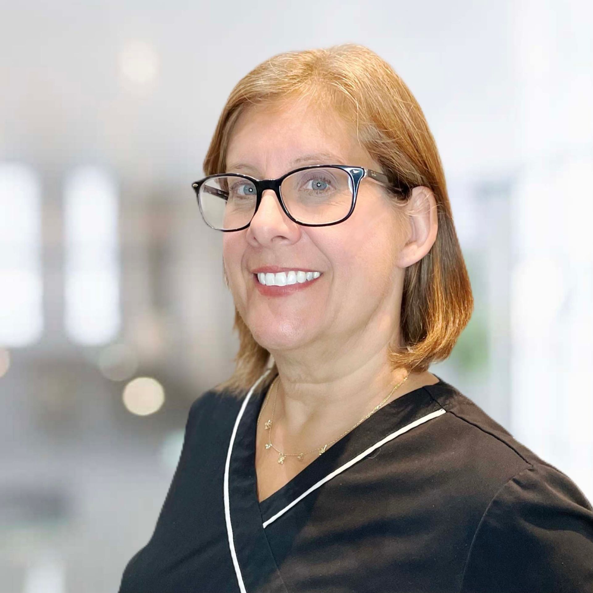 A woman wearing glasses and a black scrub top is smiling for the camera.