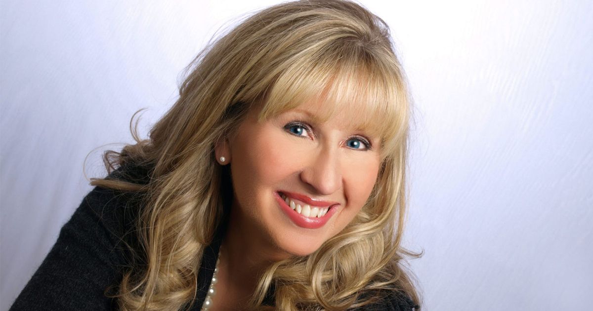 A blonde person with bangs smiling warmly against a plain white background.