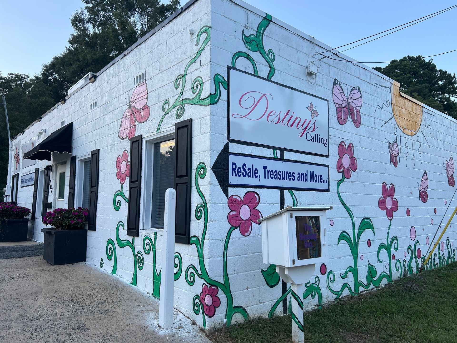 A white cinder block building painted with colorful flower and butterfly murals, featuring a sign for Destiny's Resale.