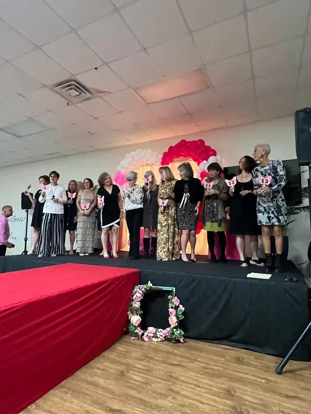 A group of people standing on a stage during a presentation, with a decorative floral display in front of the platform.