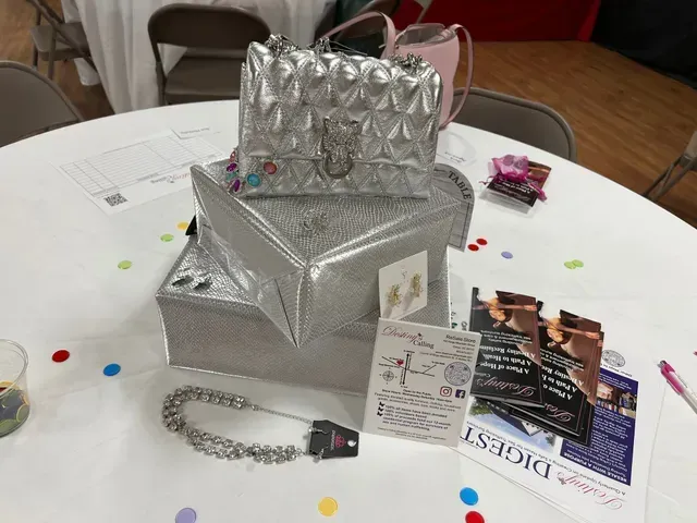 A stack of silver bags and a silver chain necklace rest on a white table with promotional brochures and cards.