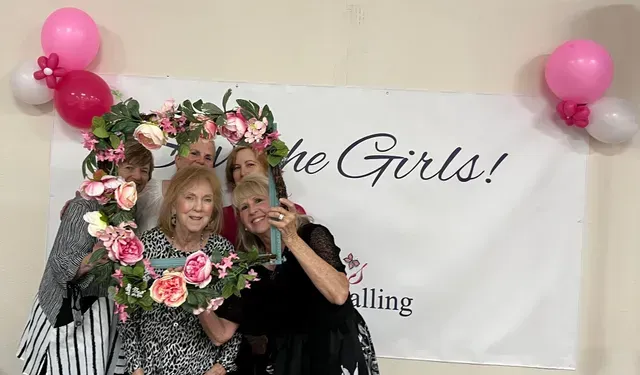 Four people pose behind a floral-decorated frame in front of a banner that reads 