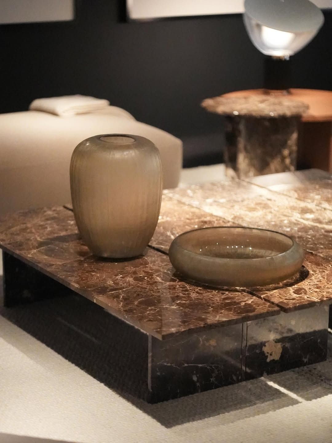 Vasi moderni in vetro e ceramica su un piedistallo di marmo, esposti in una galleria scarsamente illuminata.
