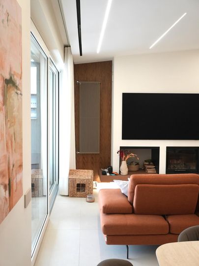 Soggiorno moderno con divano angolare color beige, grande TV a parete e finestre a tutta altezza.