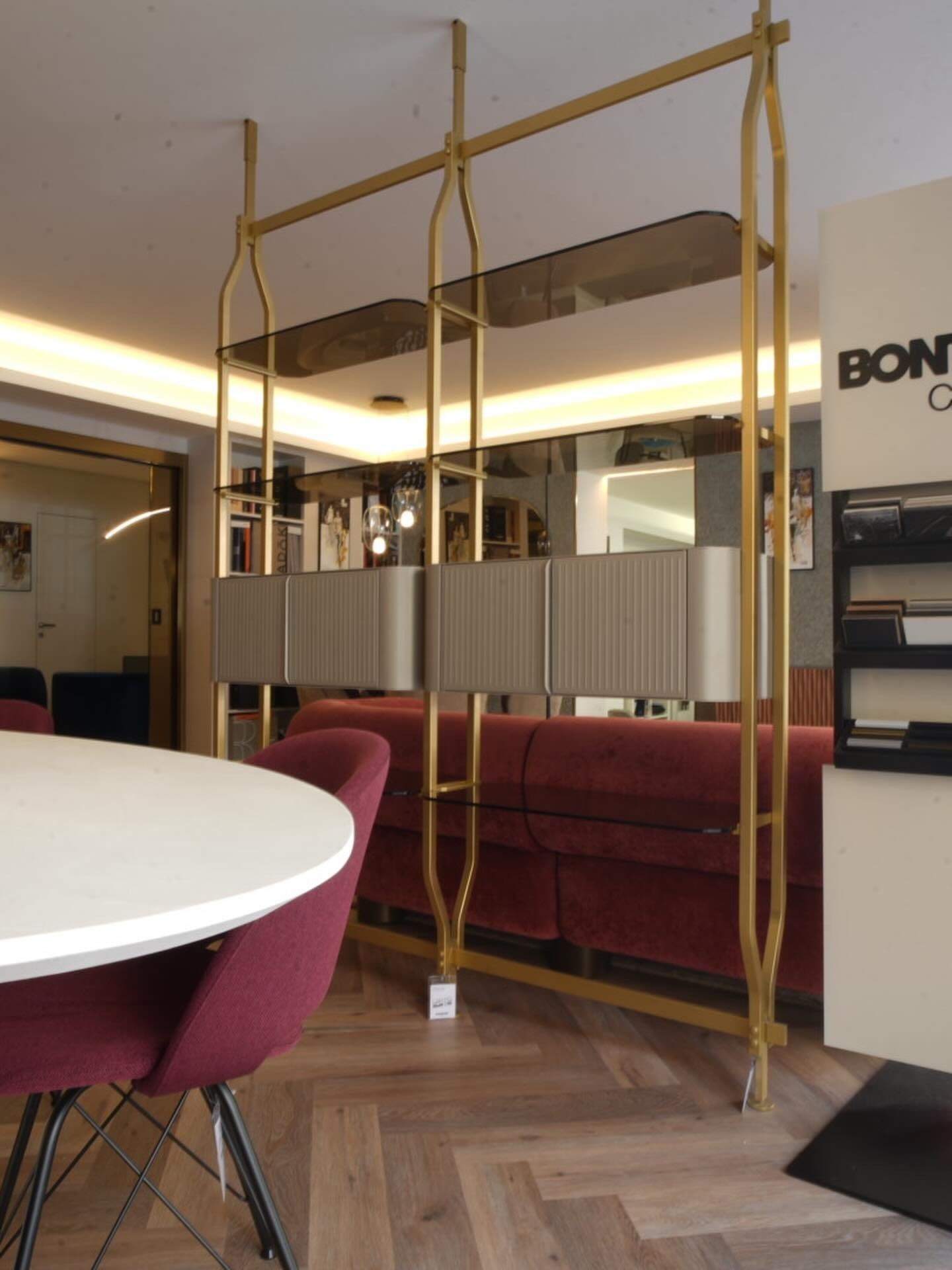 Salotto moderno con divano color bordeaux, tavolo rotondo bianco e parete a specchio con struttura a cornice dorata.