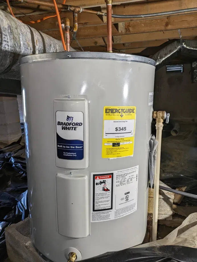 A white electric water heater is sitting in a basement.