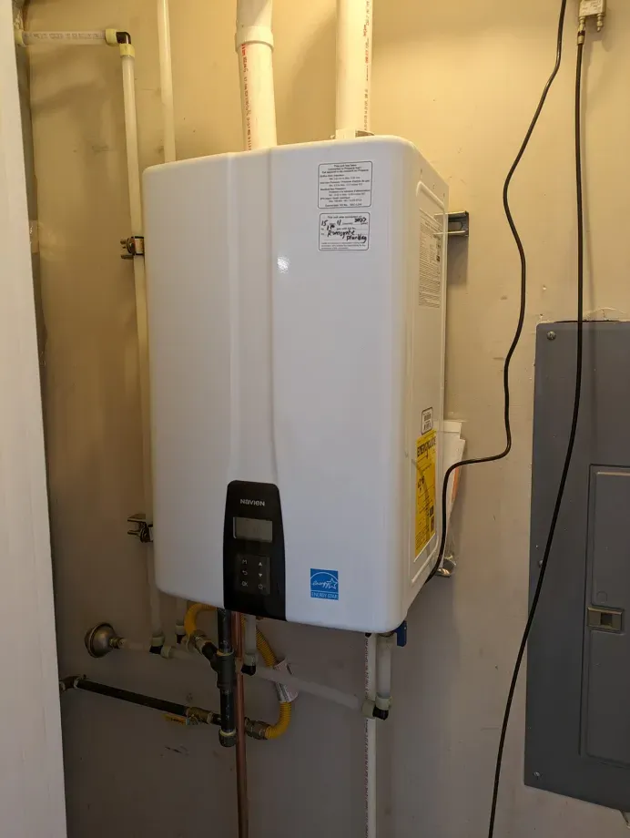 A white water heater is hanging on a wall in a room.
