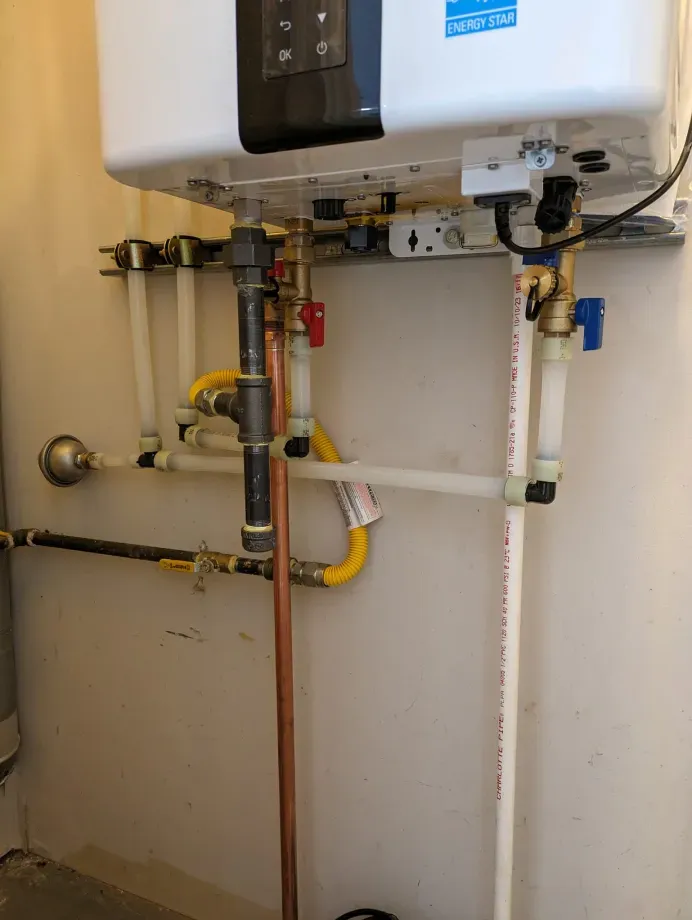A water heater is sitting on a wall next to a bunch of pipes.