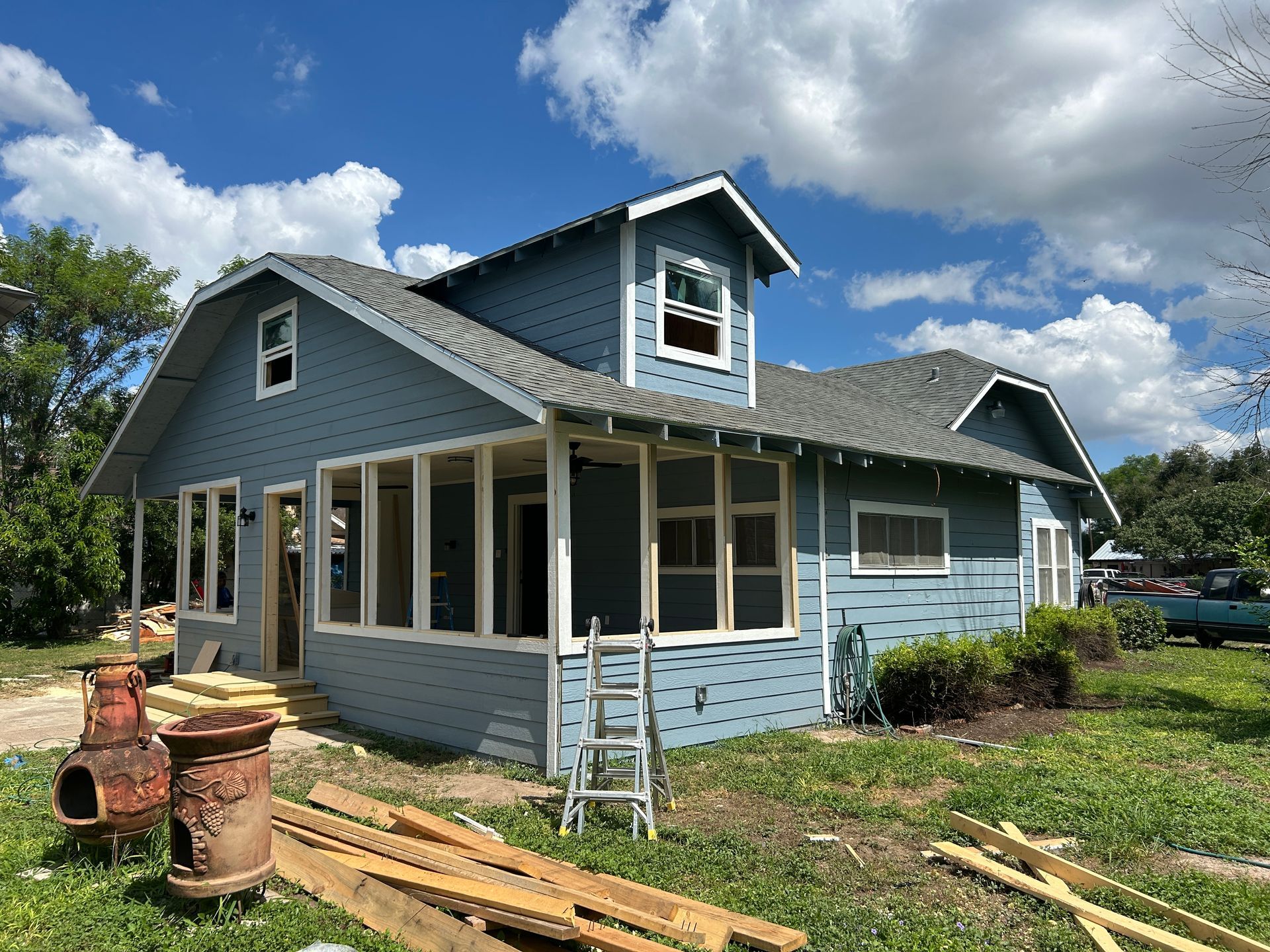 A blue house is being remodeled with a ladder in front of it.