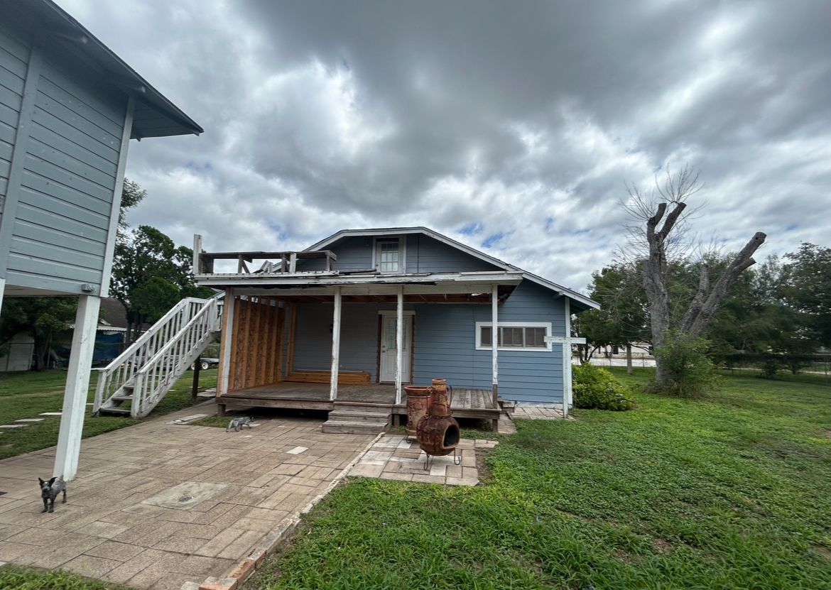 A blue house with a porch and stairs is sitting on top of a lush green field.