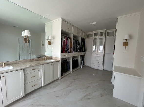 A large walk in closet with white cabinets and a large mirror.