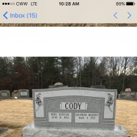 A grey granite headstone for the Cody family in a cemetery, with two names and birth dates etched into the stone.
