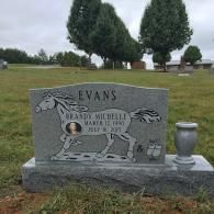 A grey granite headstone engraved with a horse, the name 