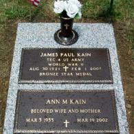 A grave marker for James Paul Kain and Ann M. Kain, featuring two bronze plaques on granite, topped with a flower vase.