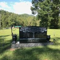 A black granite Gragg family headstone with an engraved tree design, set in a grassy field with mountains in the background.