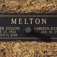 A rectangular black grave marker for the Melton family, with text showing dates for Eugene and Carolyn.