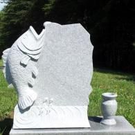 Light gray granite tombstone with a carved jumping fish on the side, set on a grass lawn with a matching stone vase.