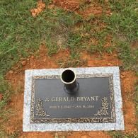 A rectangular grave marker for J. Gerald Bryant, set in grass, with an integrated metal vase in the center.