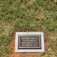 A bronze grave marker for Alvin C. Dula, dated November 22, 1936 – October 22, 2004, set in a grassy patch of dirt.