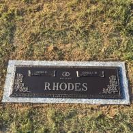 A bronze and granite memorial grave marker for the Rhodes family, set in a grassy cemetery.