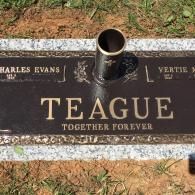 A bronze flush grave marker for the Teague family set in a grey granite base with a central metal flower vase.