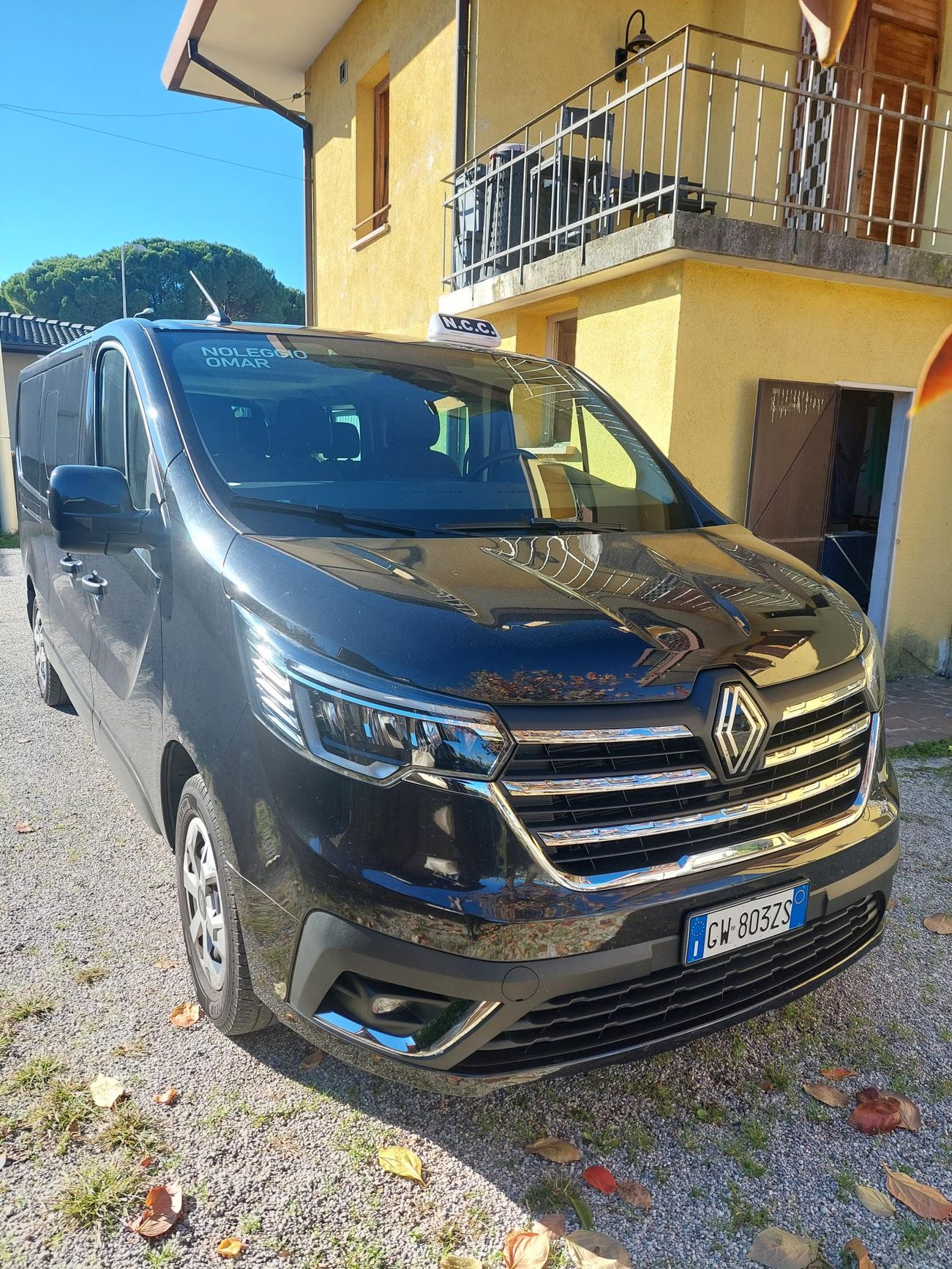 Furgone Renault Trafic grigio scuro parcheggiato sulla ghiaia di fronte a un edificio giallo con balcone.