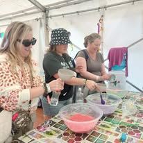 three women with smiles on their faces are mixing something colorful in bowls