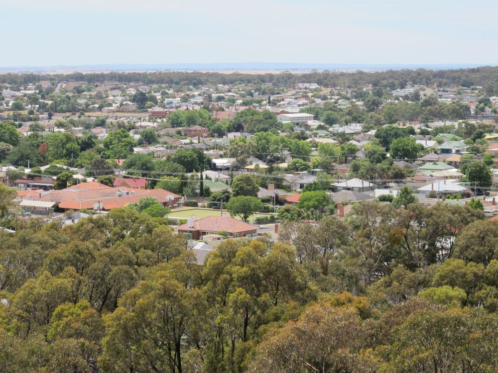 View of a town with houses, buildings, and trees from an elevated perspective on a sunny day.