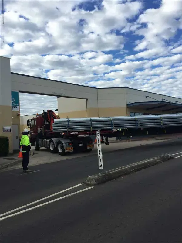 Truck Carrying Long Metal Beams, Guided by a Worker in High-vis Vest — Vision Roofing Fascia & Gutter in Hervey Bay, QLD