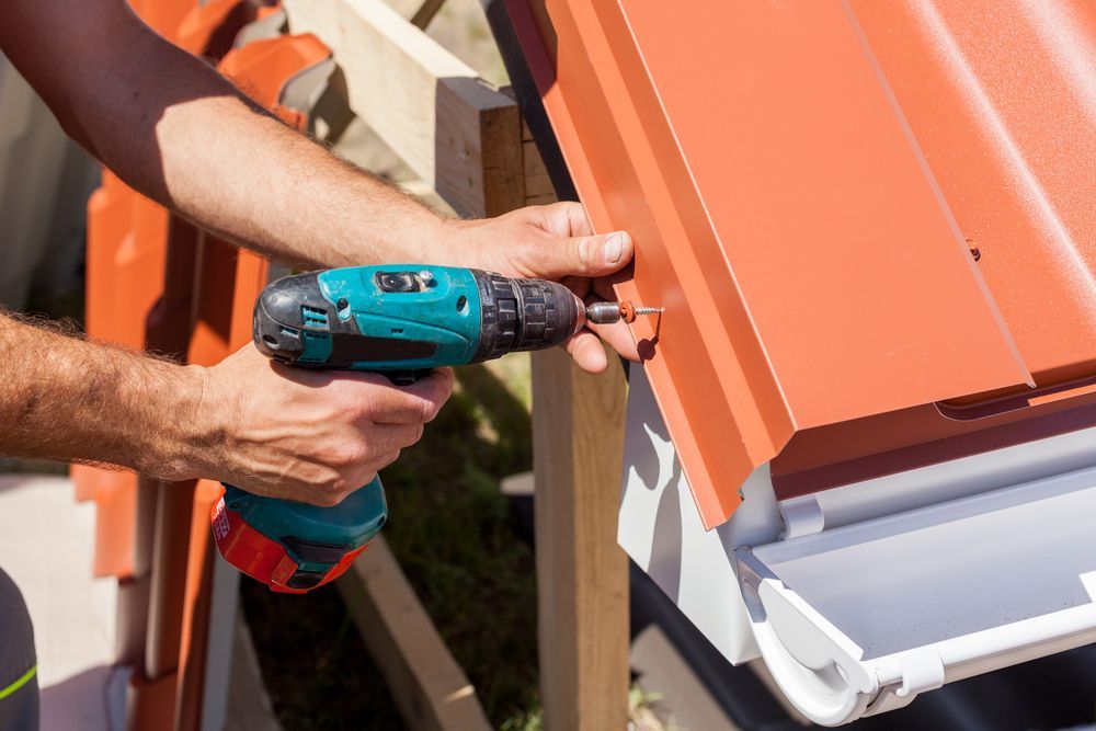Person Using a Power Drill to Install a Red Metal Roof Panel — Vision Roofing Fascia & Gutter in Howard, QLD