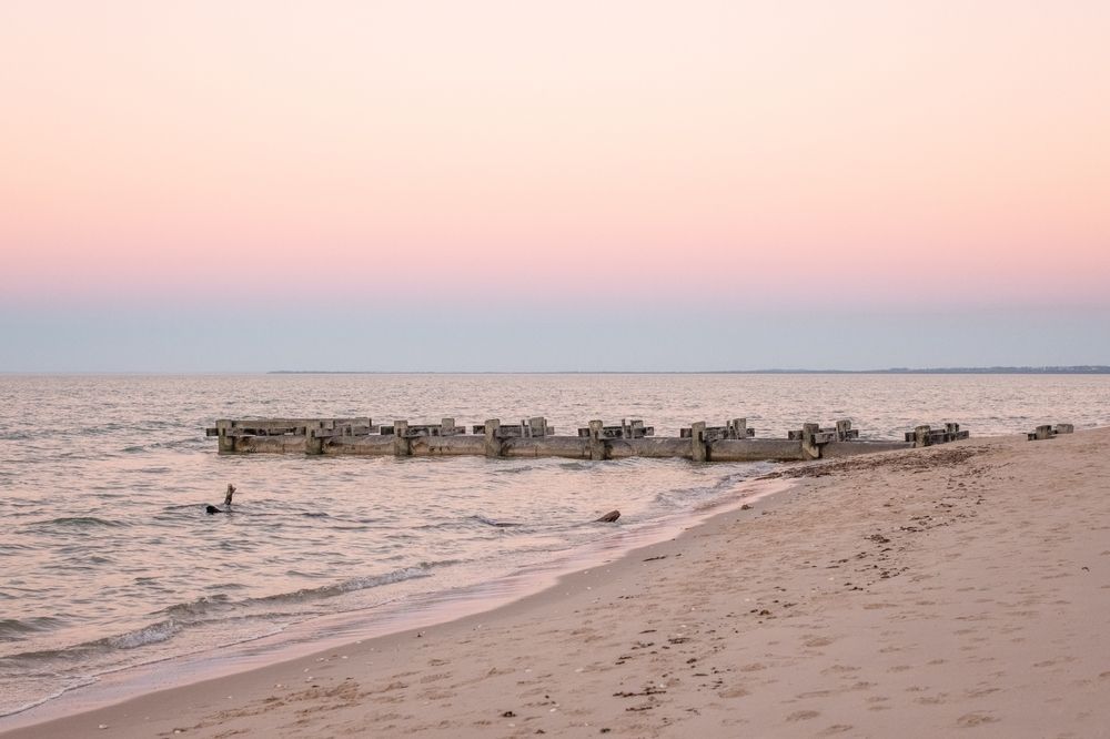 Sandy Beach and Ocean at Dusk, Weathered Wooden Structures in Water — Vision Roofing Fascia & Gutter in Burrum Heads, QLD