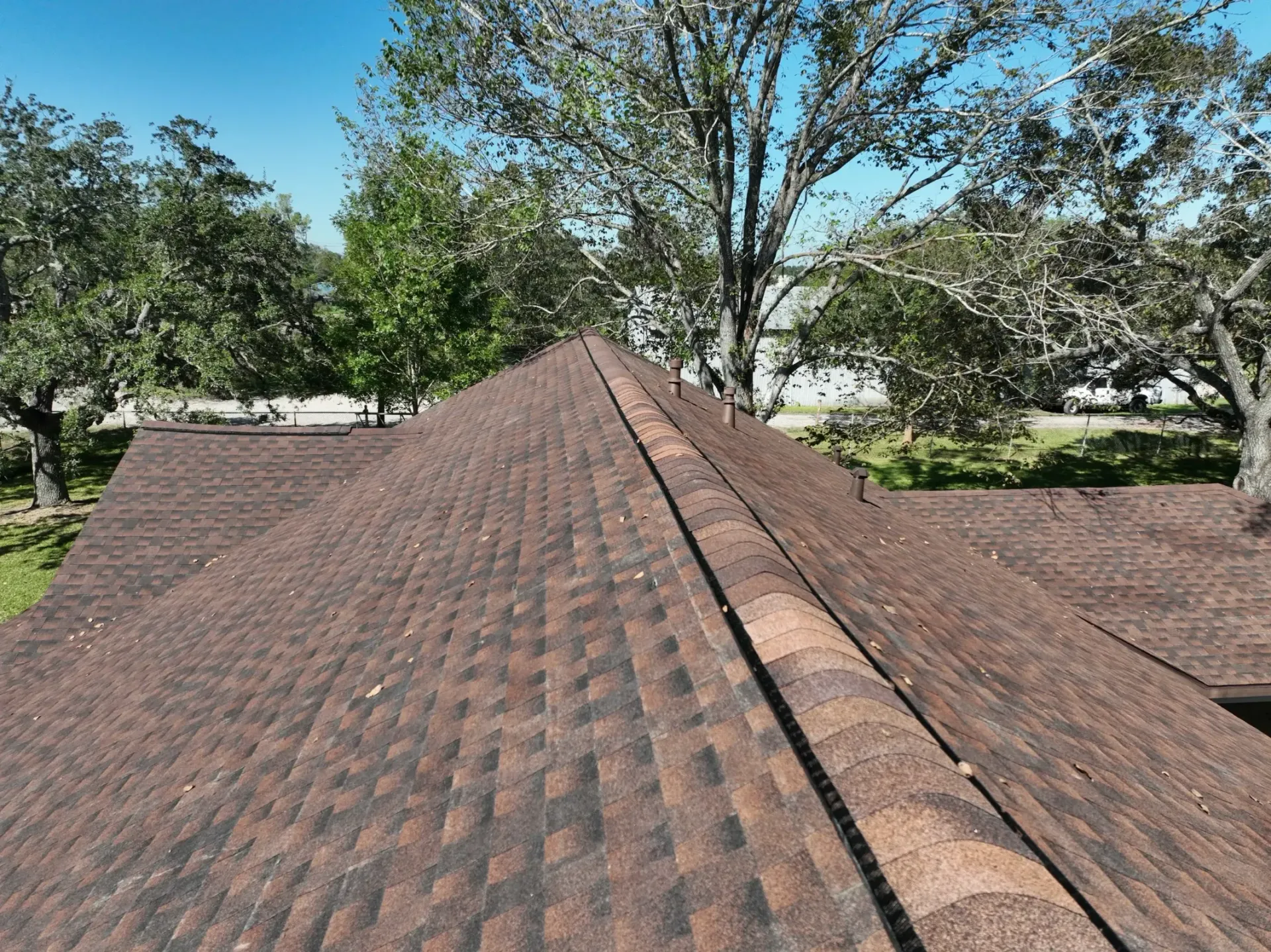 Brown shingled roof with a peak against a backdrop of green trees and blue sky. — Vision Roofing Fascia & Gutter in Hervey Bay, QLD