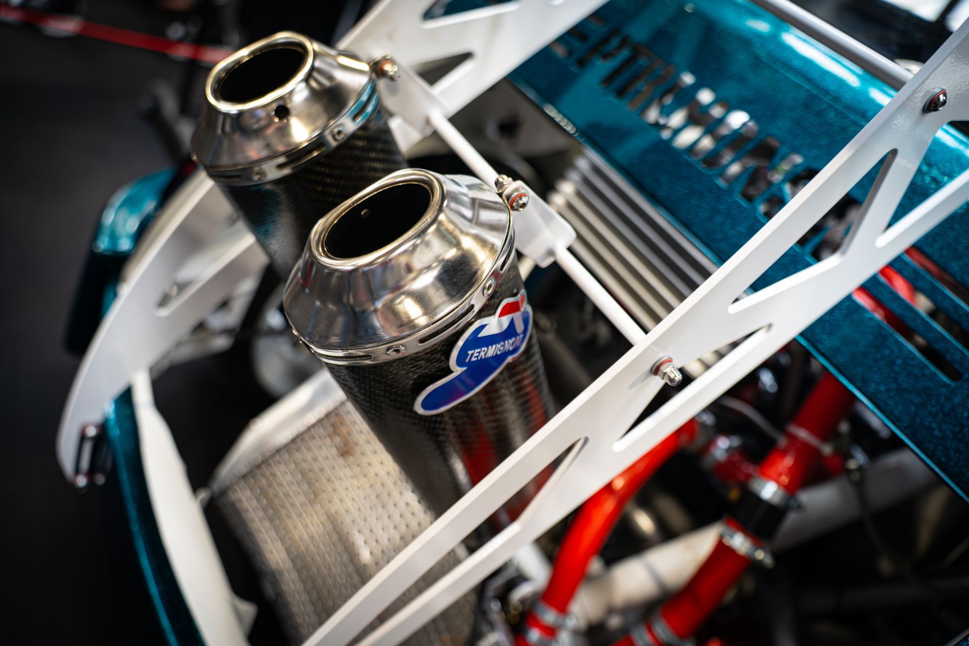 Close-up of a Fiat 500 custom exhaust system, featuring carbon fiber mufflers and white structural supports.