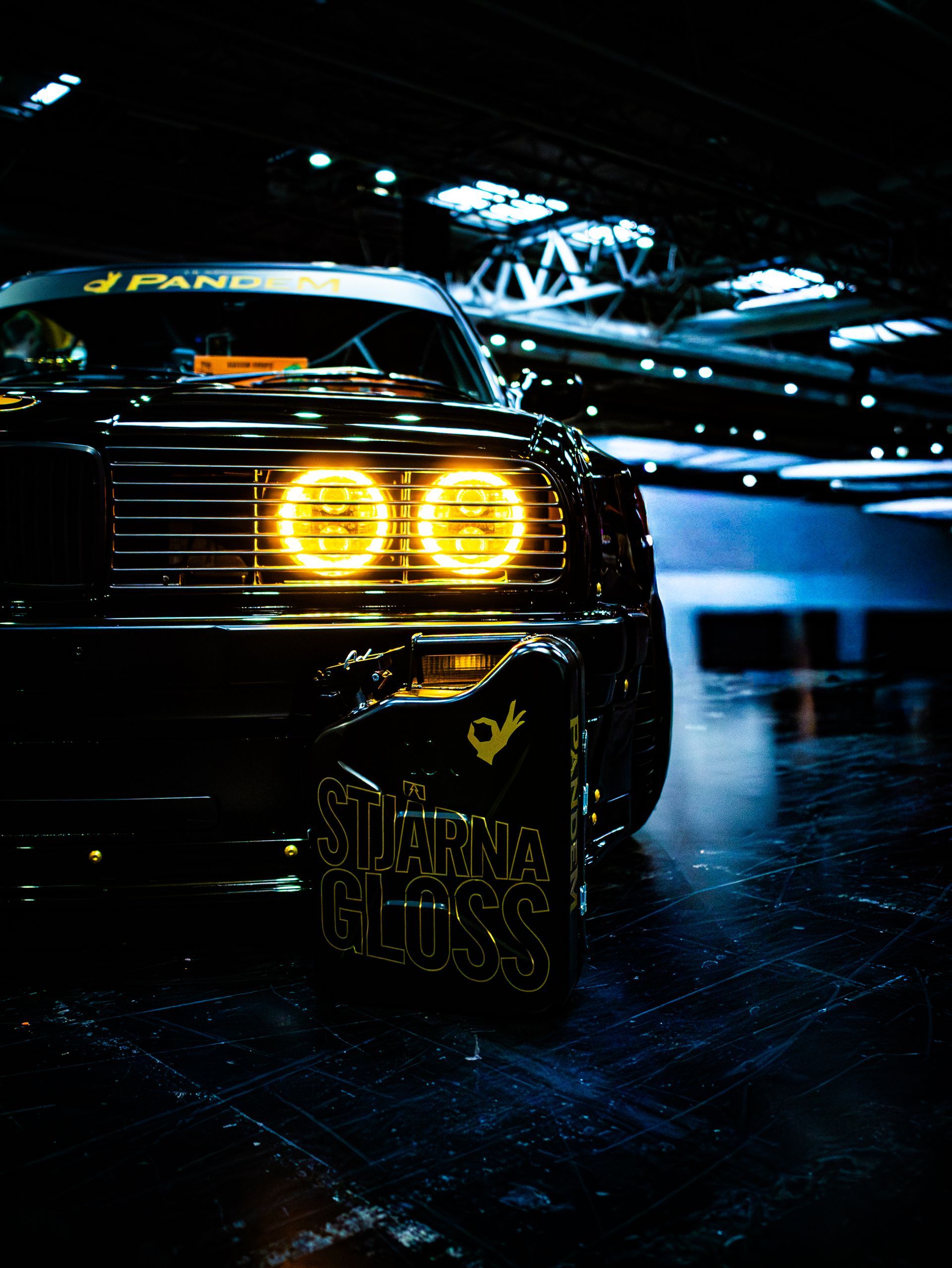 Black car with glowing yellow headlights and gold accents, set against a dark indoor background.