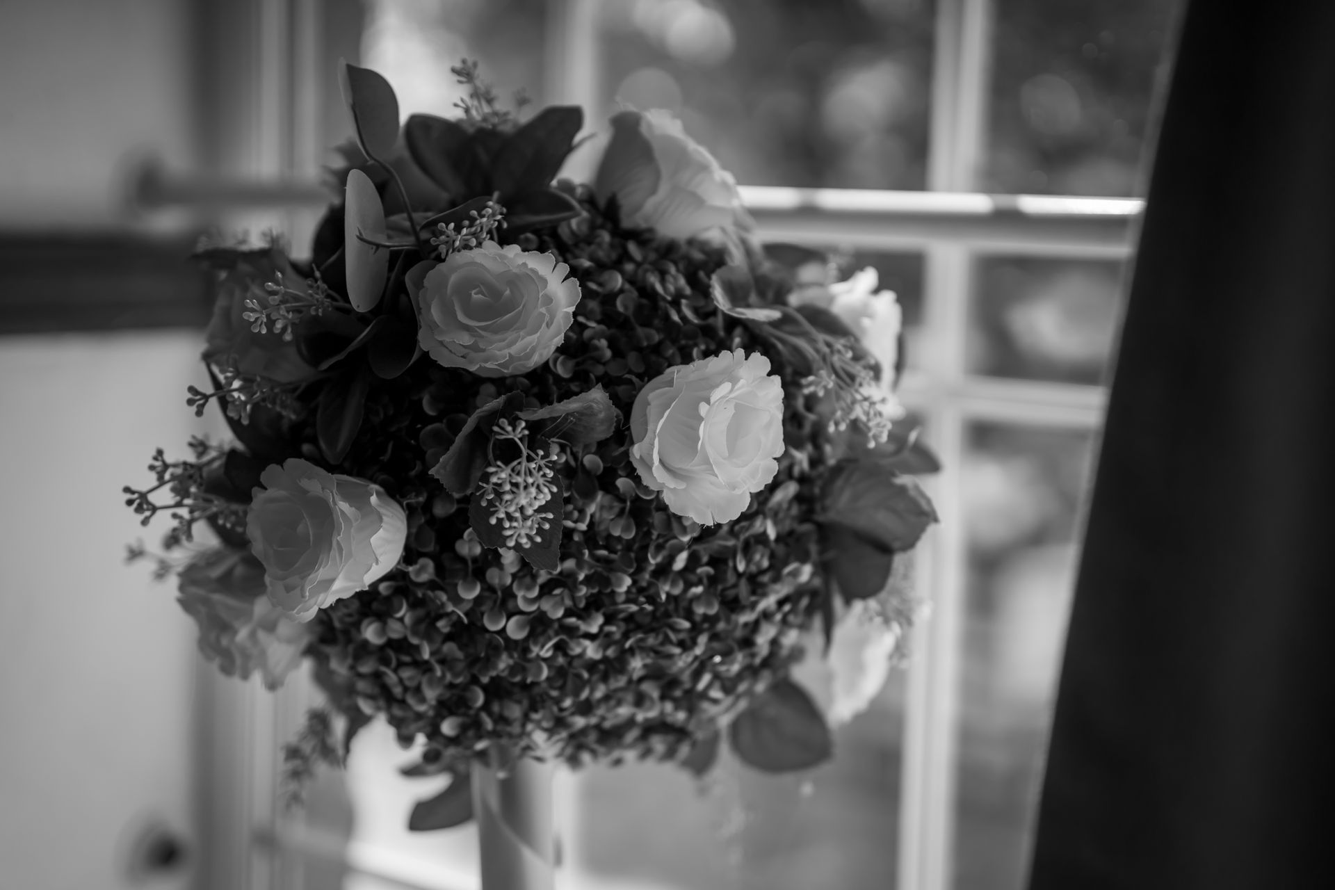 Bouquet of white roses and other flowers, placed in front of a window. Black and white.