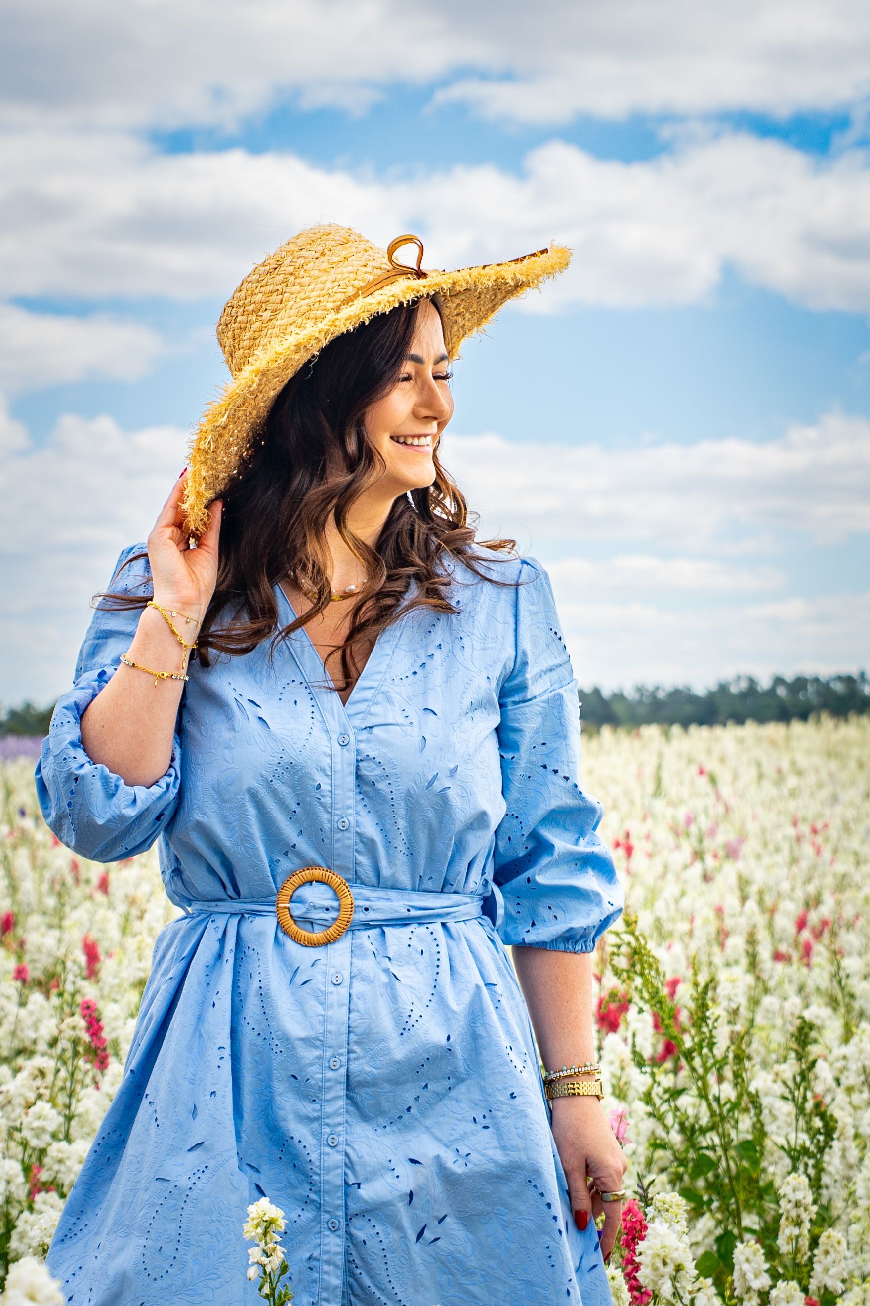 Woman in blue dress and straw hat smiles in a field of flowers.