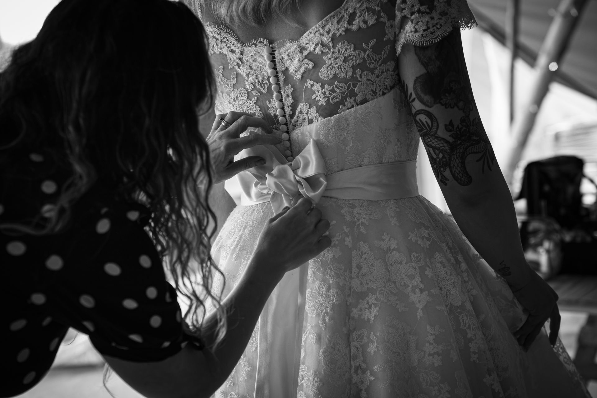 Woman in wedding dress having back fastened by another woman.