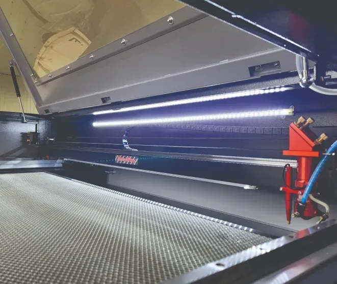 Interior view of a laser cutter machine with bright LED lights illuminating the cutting area.