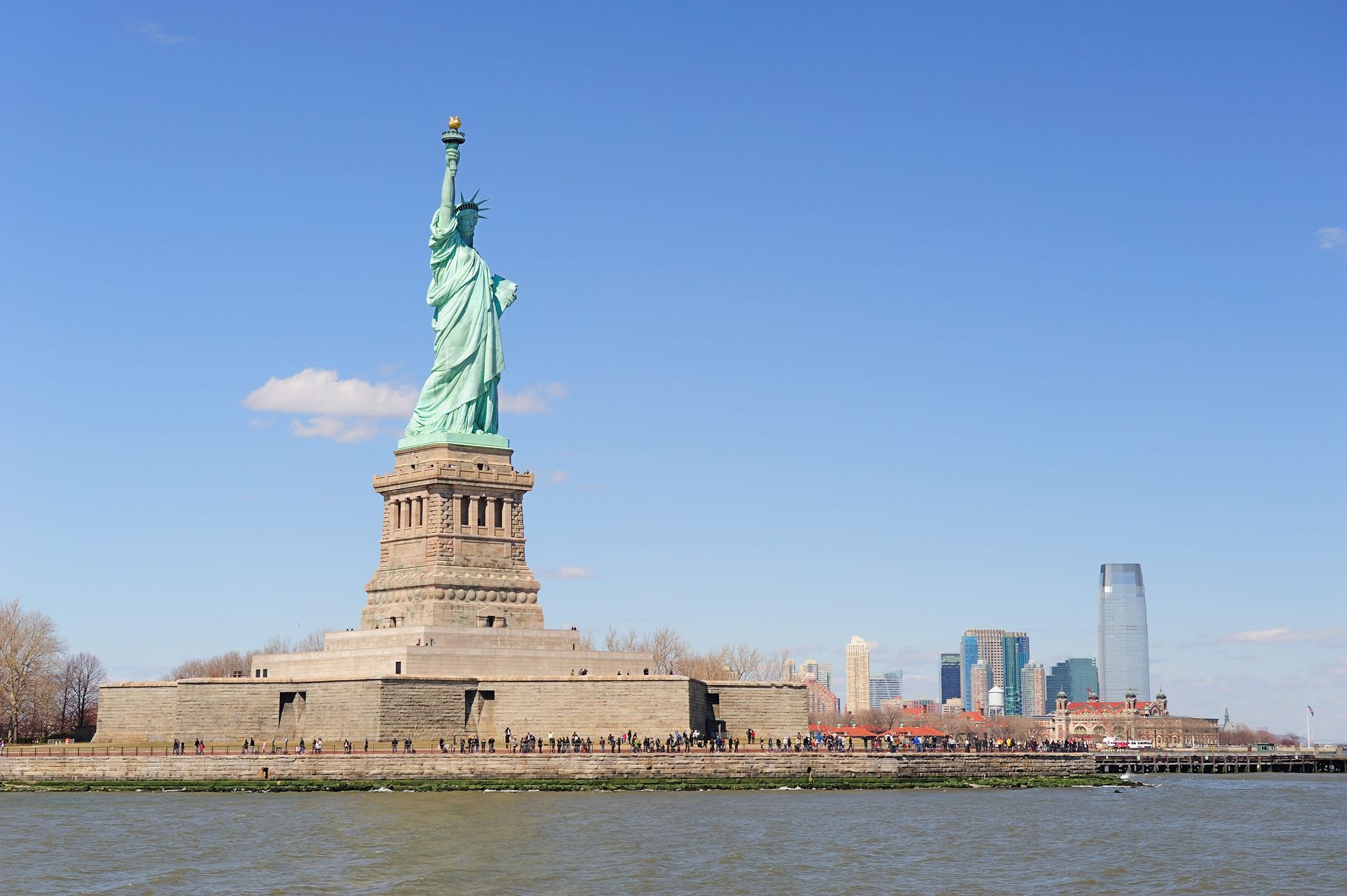 Statue of Liberty on Liberty Island, New York City, against a blue sky, with a city skyline in the background.