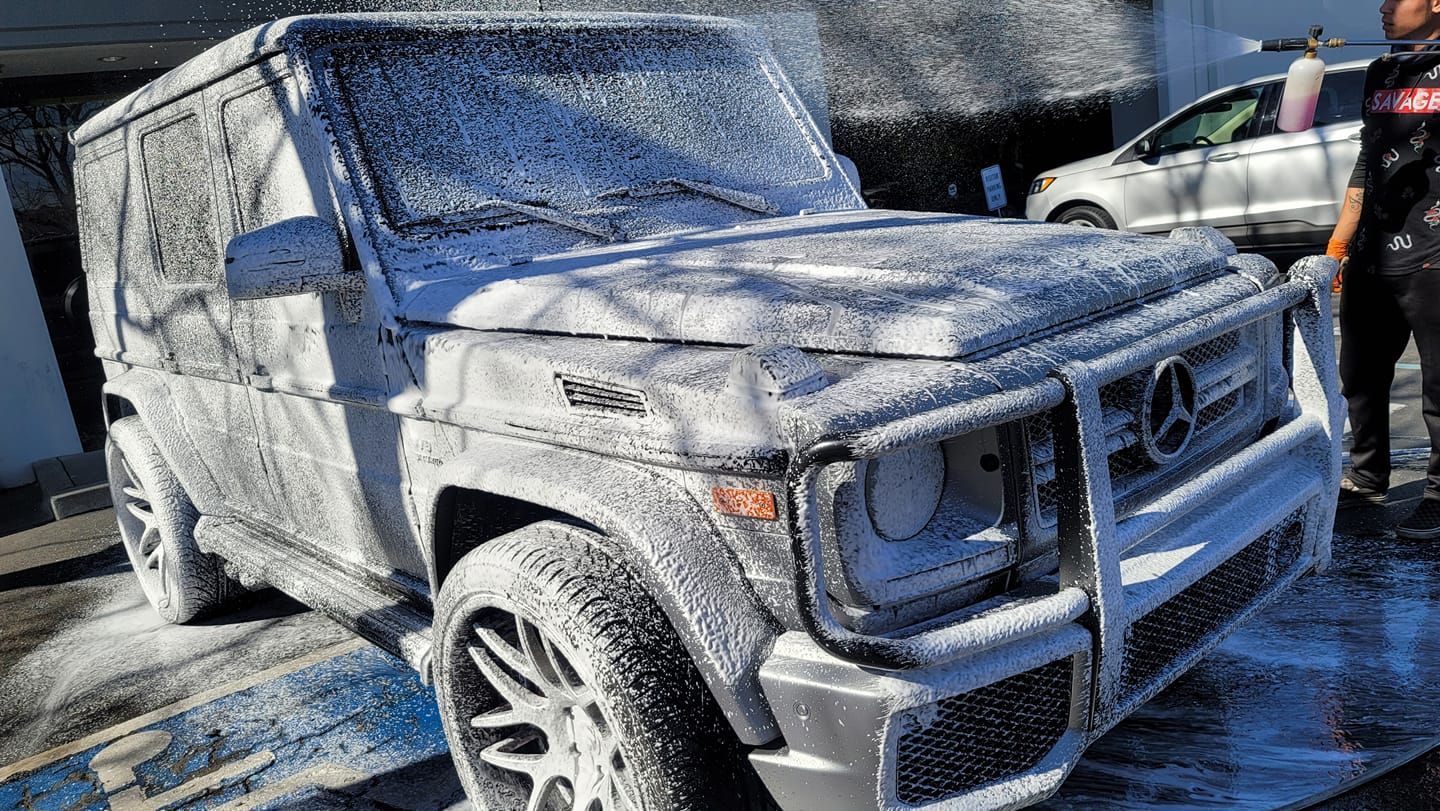 A mercedes benz g63 is covered in foam at a car wash.