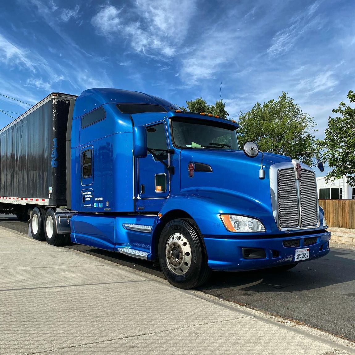 A blue semi truck with a black trailer is parked on the side of the road.