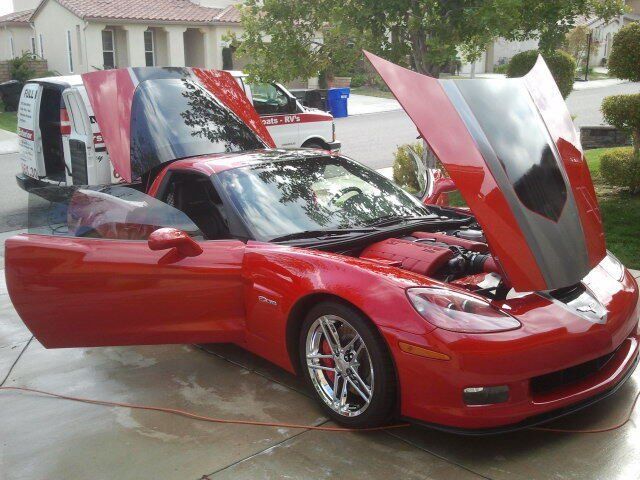 A red sports car with the hood up is parked in a driveway
