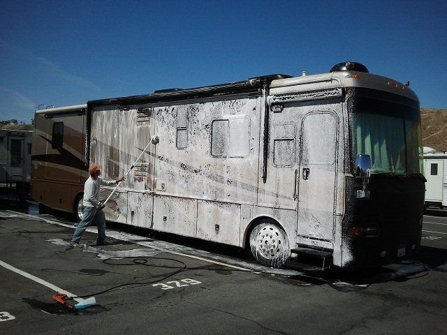 A man is washing a rv in a parking lot